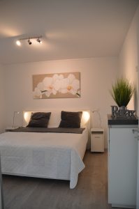 Belegungsplan Ferienhaus Aldenburg - Das Schlafzimmer ist mit einem Boxspringbett, einer Kommode mit Schubläden, zwei Nachttischen sowie einem Kleiderschrank mit Schiebetüren ausgestattet.